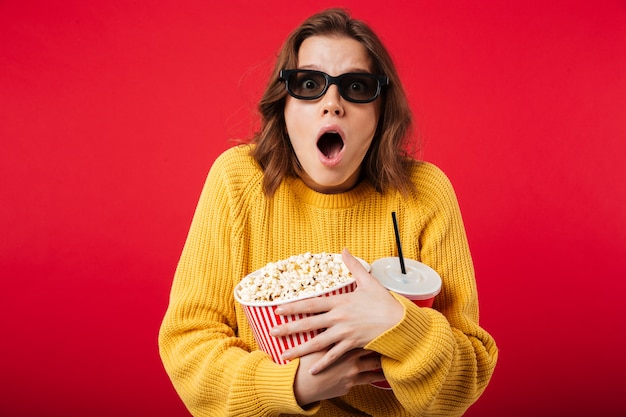 Portrait of a shocked woman in sunglasses holding popcorn