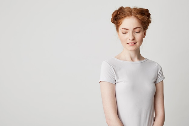 Free photo portrait of shy young pretty redhead girl with buns looking down smiling .