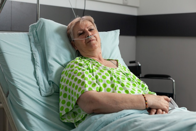 Portrait of sick pensioner woman looking into camera while resting in bed