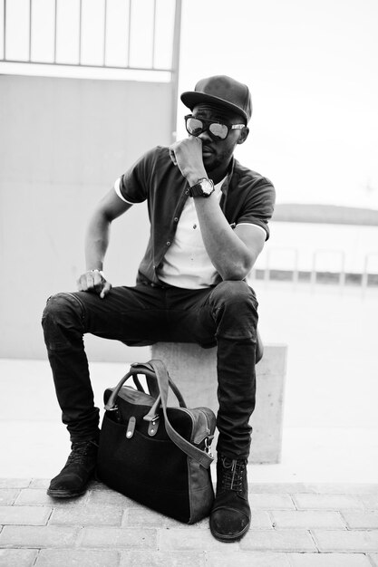 Portrait of sitting stylish african american man wear on sunglasses and cap outdoor Street fashion black man