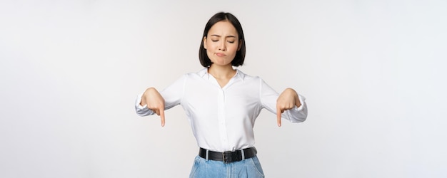 Free Photo portrait of skeptical disappointed asian businesswoman korean girl pointing and looking down with doubts standing against white background