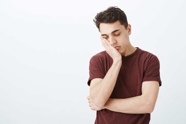 Portrait of sleepy charming guy in casual outfit, leaning face on palm and closing eyes, feeling tired and exhausted, having lack of sleep