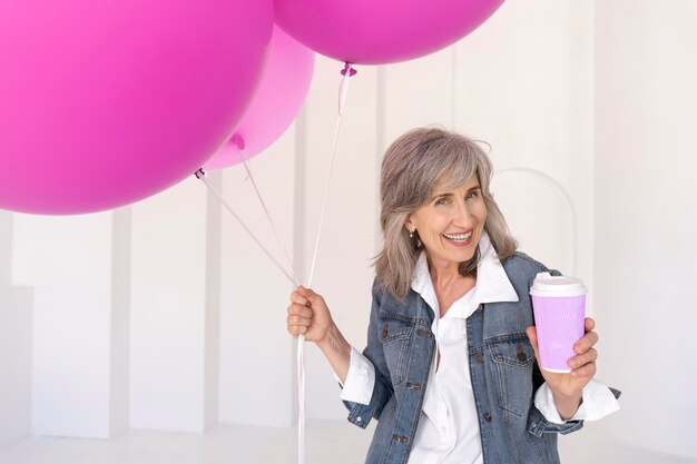 Portrait of smiley senior woman holding cup and pink balloons