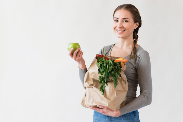 Portrait of smiley woman holding bag with fruits and vegetables