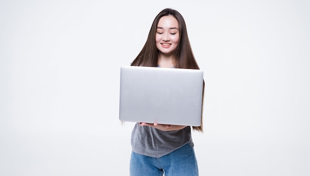 Portrait of a smiling asian woman holding laptop computer isolated on gray wall