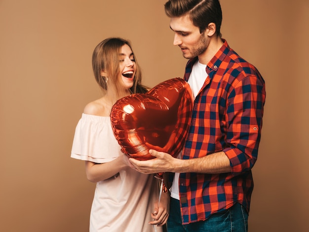 Free photo portrait of smiling beautiful girl and her handsome boyfriend holding heart shaped balloons and laughing. happy couple in love. happy valentine's day