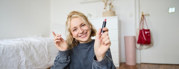 Portrait of smiling beautiful woman in her room sitting and showing lipstick recommending favourite