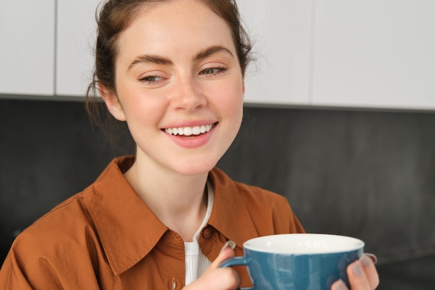 Free Photo portrait of smiling beautiful woman at home drinking coffee enjoys delicious taste of freshly brewed