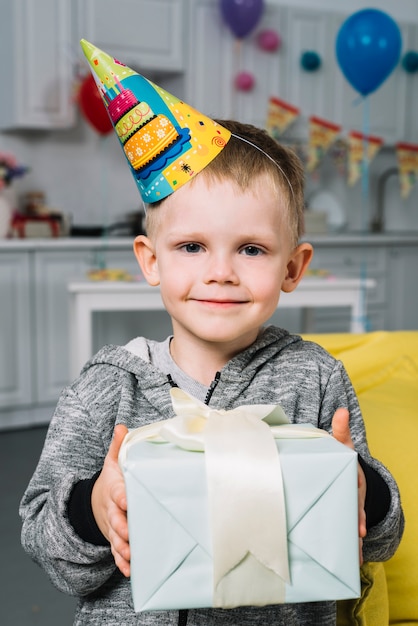 Free Photo portrait of a smiling birthday boy holding wrapped gift box in hand