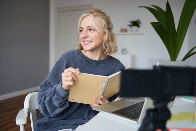 Free Photo portrait of smiling blond woman sitting in bedroom using laptop and digital camera recording video