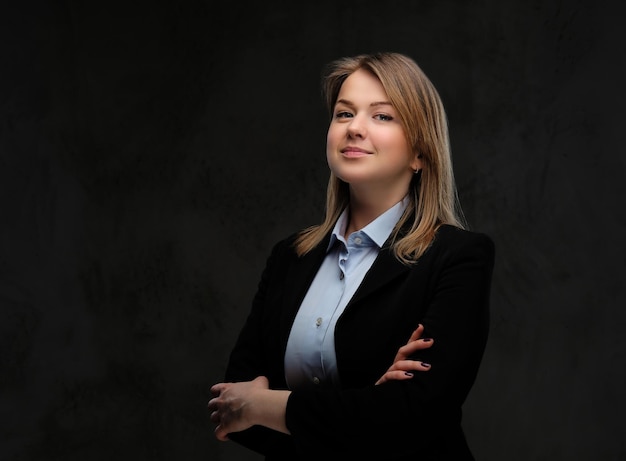 Portrait of a smiling blonde businesswoman formal dressed standing with crossed arms. Isolated on a dark textured background.