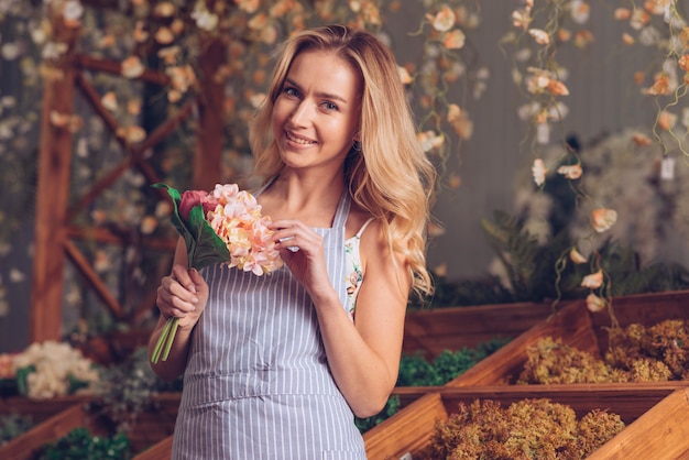 Free photo portrait of smiling blonde female florist holding flower bouquet in hand