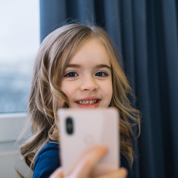 Portrait of a smiling blonde girl taking self portrait on mobile phone