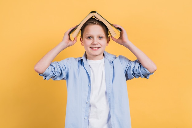 Free Photo portrait of a smiling boy holding book over his head looking to camera against yellow background