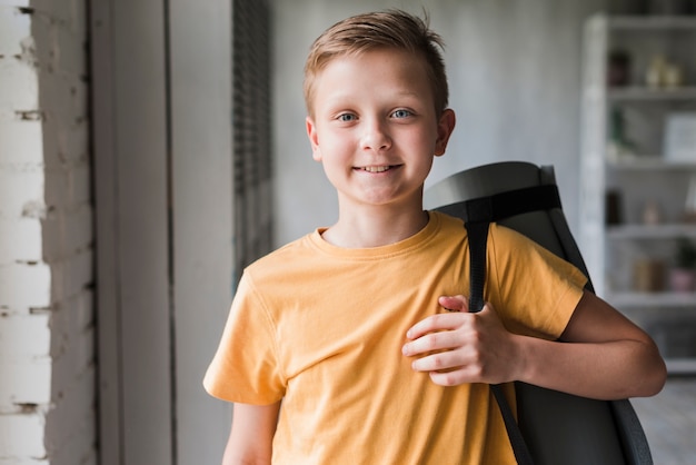 Free photo portrait of a smiling boy holding exercise mat on his shoulder