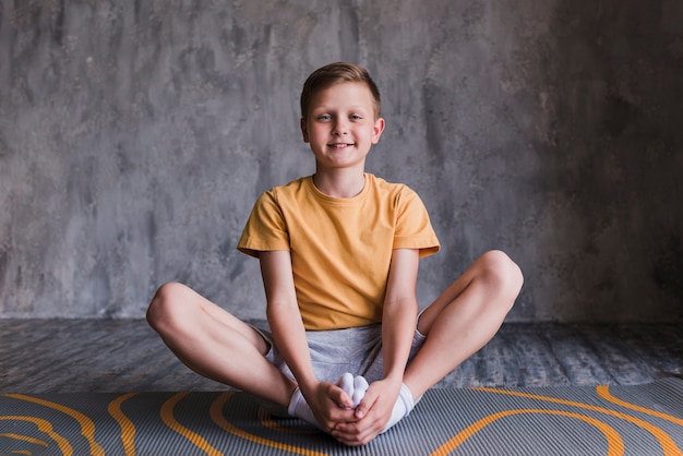 Free photo portrait of a smiling boy sitting on exercise mat looking at camera