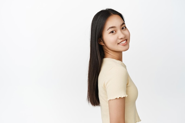 Portrait of smiling brunette asian girl with shiny healthy hair looking at camera confident and happy standing over white background