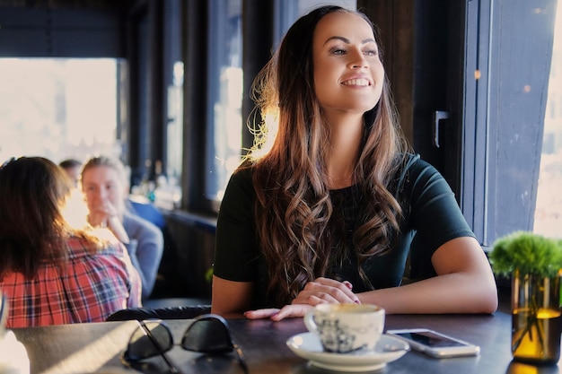 Portrait of smiling brunette woman drinks morning coffee in a cafe.