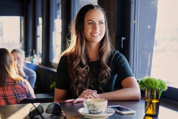 Portrait of smiling brunette woman drinks morning coffee in a cafe.