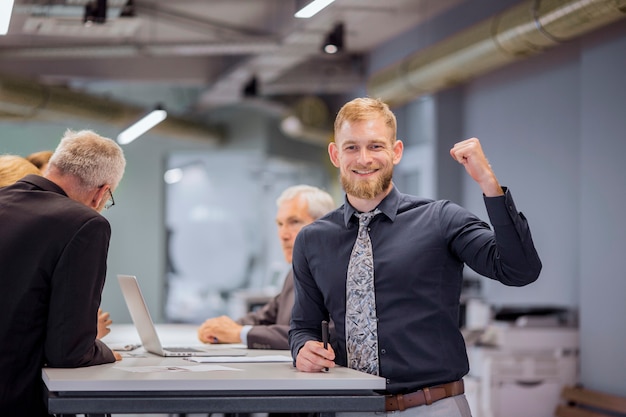 Portrait of smiling businessman clenching his fist while team discussing in the background