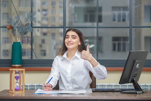 Portrait of a smiling businesswoman sitting at the desk and gesture thumb up