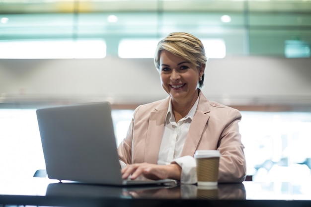 Portrait of smiling businesswoman using laptop in waiting area