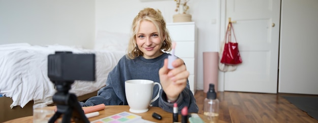 Free photo portrait of smiling charismatic woman puts on lip gloss drinks tea records video on digital camera