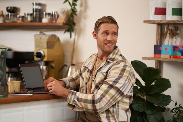 Free photo portrait of smiling charismatic young man digital nomad working from cafe sitting in coffee shop