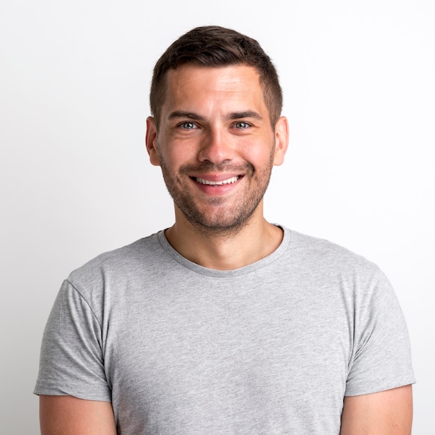 Portrait of smiling charming young man in grey t-shirt standing against plain background