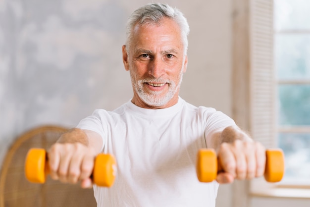 Free photo portrait of smiling elderly man holding dumbbells