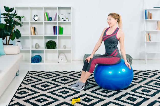 Portrait of a smiling fitness young woman sitting on blue pilates ball looking away