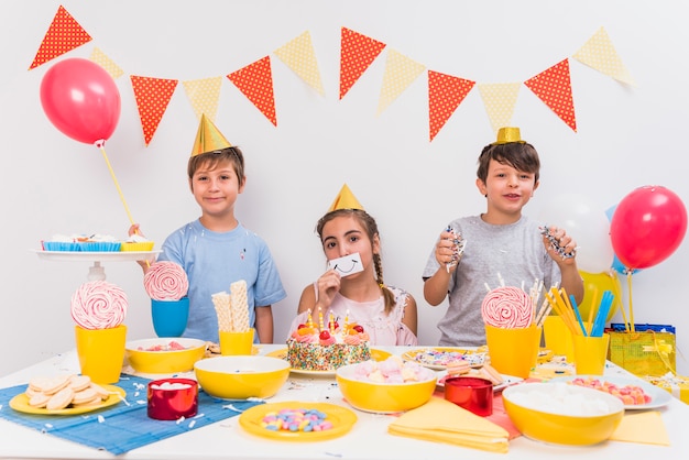 Portrait of smiling friends holding smiley card; balloon and confetti with food on table