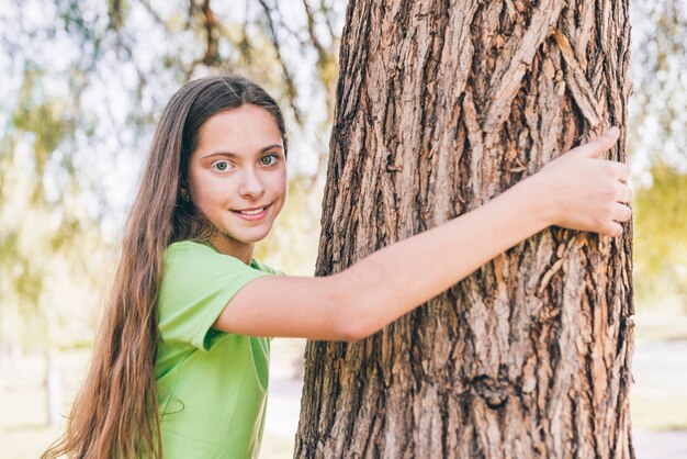 Portrait of a smiling girl embracing tree trunk