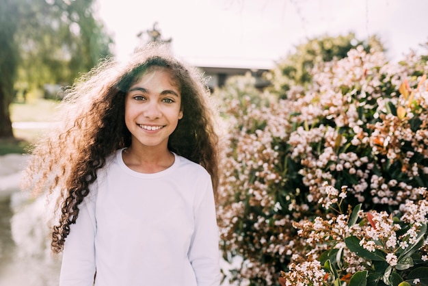 Portrait of a smiling girl looking at camera standing in front of flowers plant