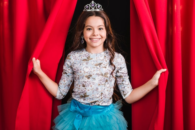 Portrait of smiling girl looking out from red curtain