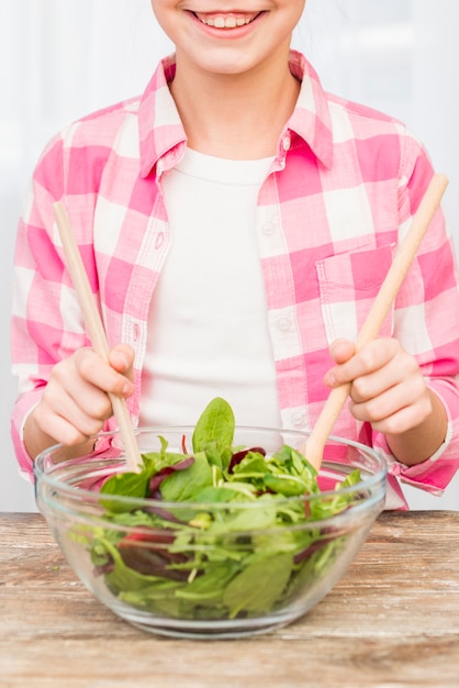 Free photo portrait of a smiling girl preparing salad with wooden spoon in the glass bowl