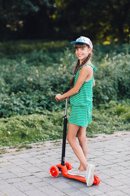 Free photo portrait of smiling girl wearing cap standing on scooter