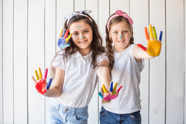 Free Photo portrait of smiling girls wearing headband showing colorful painted hands against wooden wall