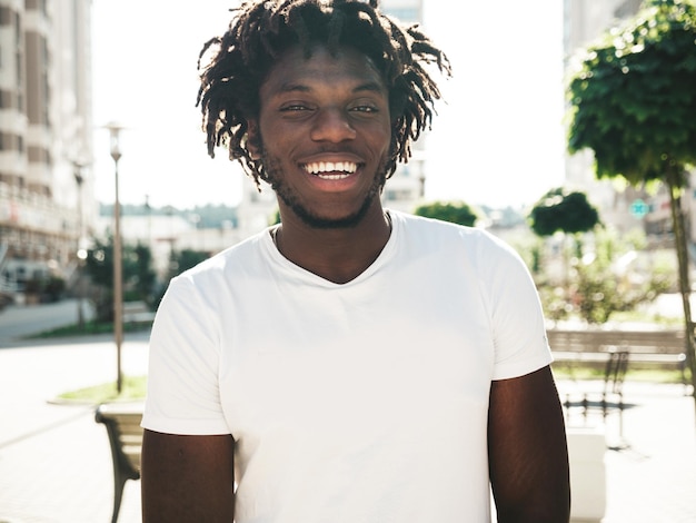 Free photo portrait of smiling handsome hipster modelunshaven african man dressed in white summer tshirt and jeans fashion male with dreadlocks hairstyle posing on the street background