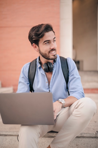 Portrait of a smiling handsome man with laptop looking away