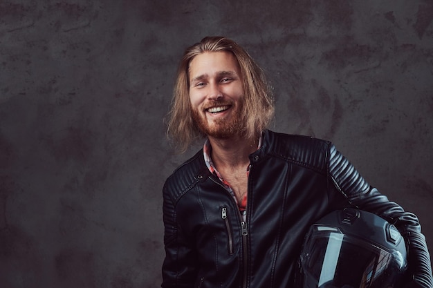 Free Photo portrait of a smiling handsome stylish redhead biker in a black leather jacket, holds motorcycle helmet, posing in a studio. isolated on a dark background.