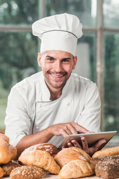 Free photo portrait of smiling male baker using digital tablet with many baked breads