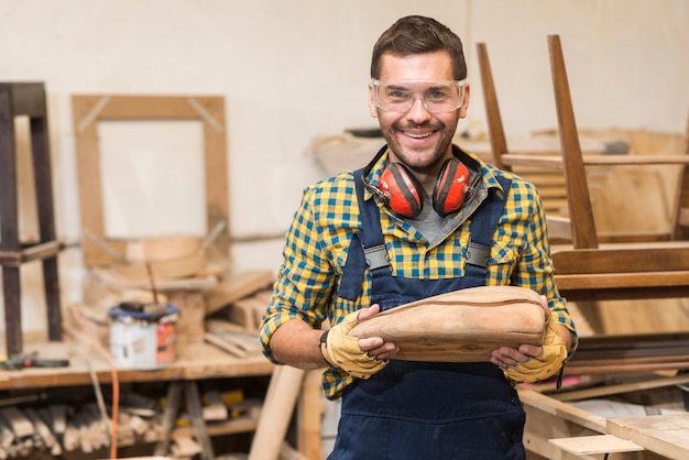 Free photo portrait of smiling male carpenter holding incomplete wooden model