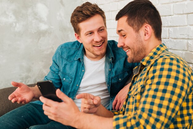 Portrait of a smiling male friend showing something on smartphone to his friend