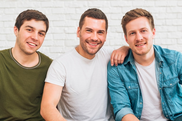 Portrait of smiling male friends looking at camera against white brick wall