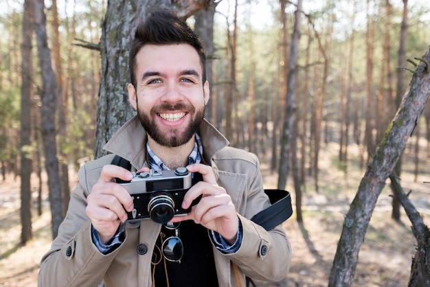 Free photo portrait of a smiling male hiker holding camera in hand looking at camera