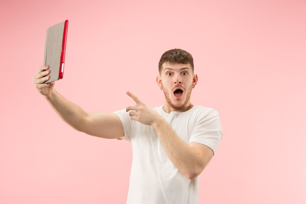 Portrait of smiling man pointing at laptop with blank screen isolated on pink studio background. Human emotions, facial expression concept and advertising concept.