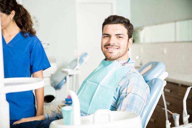 Portrait of smiling man sitting on chair while female dentist working in clinic