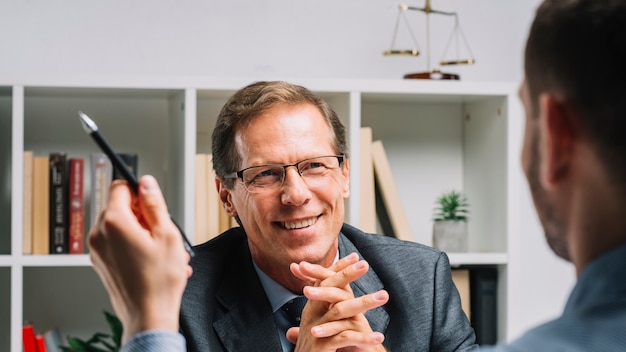 Free photo portrait of smiling mature lawyer sitting with business customer holding pen