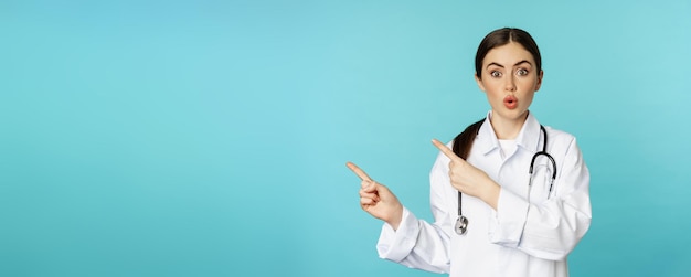 Free Photo portrait of smiling medical worker girl doctor in white coat with stethoscope pointing fingers left